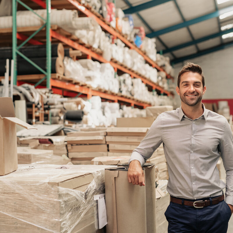 Man smiling while leaning against cardboard boxes in a large warehouse
